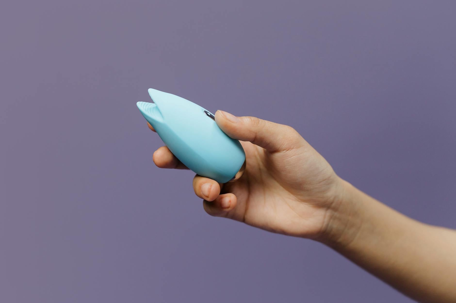 A teal silicone vibrator resting on smooth white silk fabric