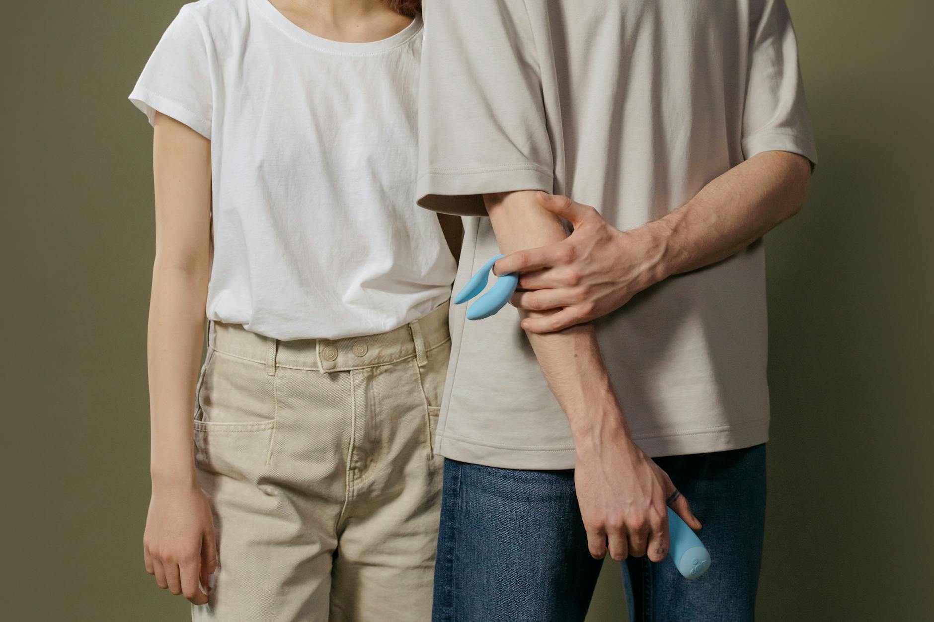 A young couple standing together indoors, holding a blue vibrator, symbolizing modern intimacy and partnership.